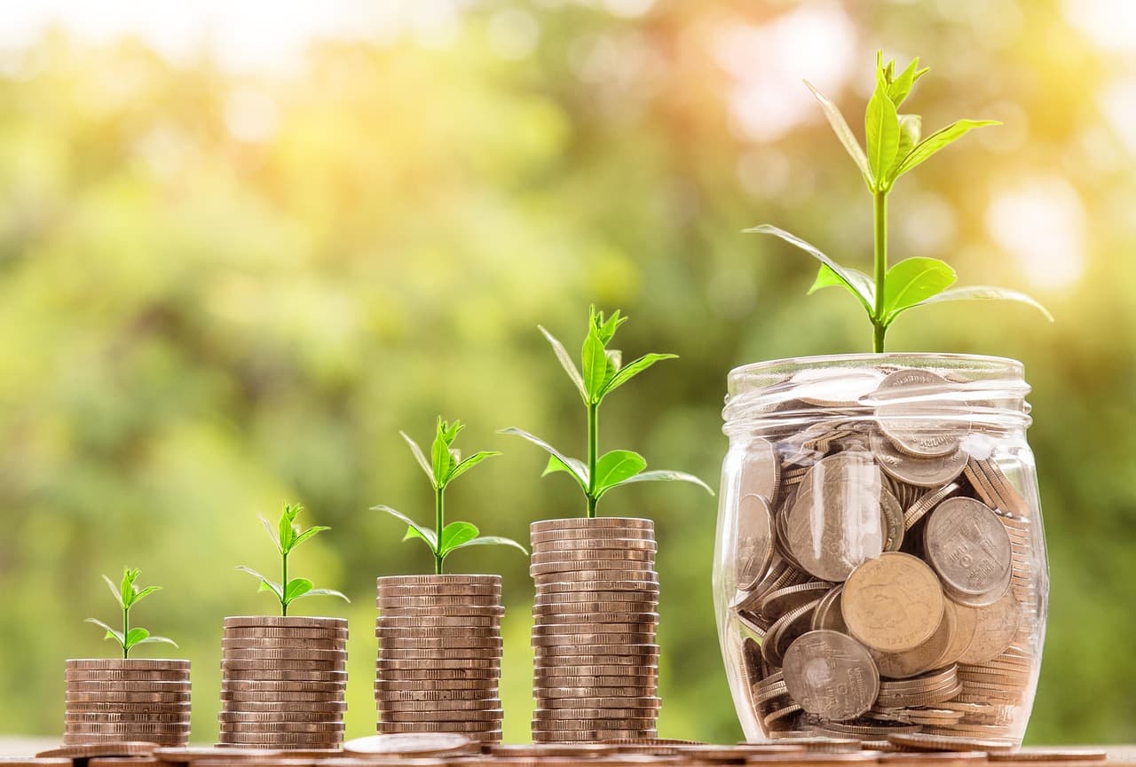 Stacks of coins with seedlings growing from them, beside a glass jar of coins