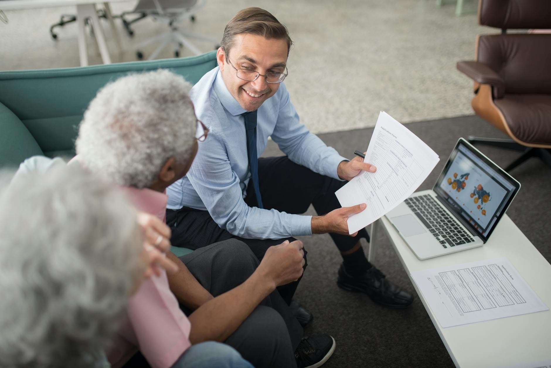 An adviser going through an application form with an older couple, a laptop open beside them