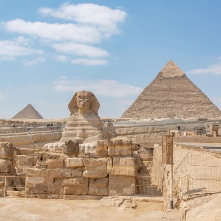 Iconic view of the Great Sphinx and Giza Pyramids in Egypt under a clear blue sky.