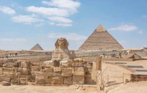 Iconic view of the Great Sphinx and Giza Pyramids in Egypt under a clear blue sky.