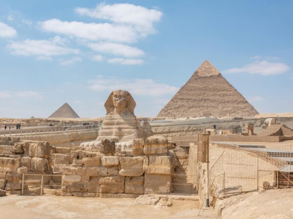egypt} Iconic view of the Great Sphinx and Giza Pyramids in Egypt under a clear blue sky.