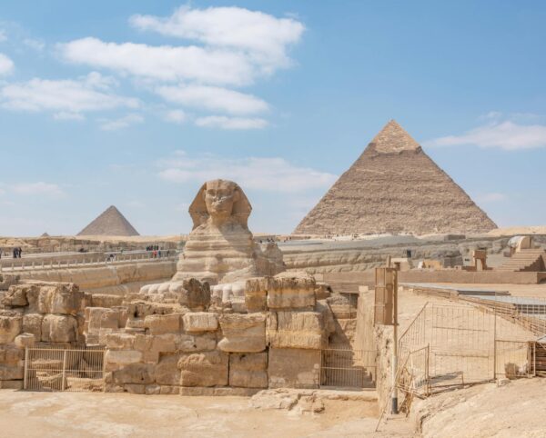 egypt} Iconic view of the Great Sphinx and Giza Pyramids in Egypt under a clear blue sky.