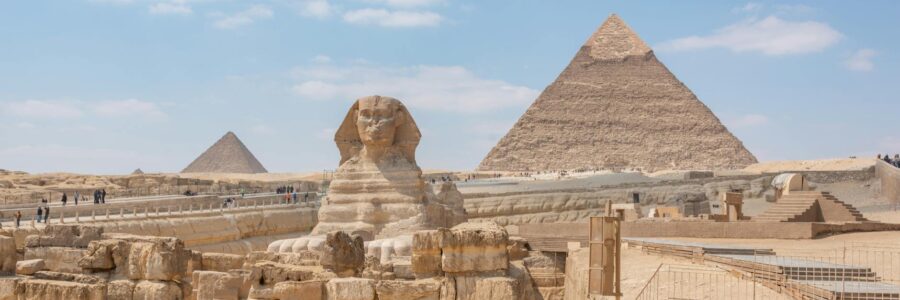Iconic view of the Great Sphinx and Giza Pyramids in Egypt under a clear blue sky.
